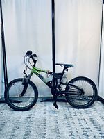 Full side view of the green and black kids mountain bike on carpeted floor with white background