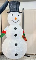 Front view of the illuminated snowman decoration with black hat, carrot nose, smiling face, and black buttons. Shows the texture and LED lights glowing.