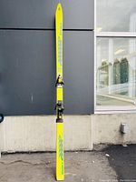 Full length view of a single neon yellow Salomon ski with blue geometric pattern and binding mounted.