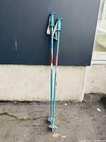 Pair of used blue and red ski poles standing against concrete and dark wall outside