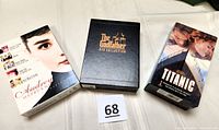Photo showing three boxed movie collections: Audrey Hepburn DVD collection, The Godfather DVD collection, Titanic VHS set.
