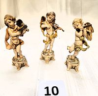 Front view of all three Fontanini cherub angel figurines showing their detailed faces, wings, instruments, and stools.