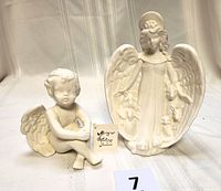 Two glazed bisque angel figurines including the small sitting cherub and standing guardian angel from front view