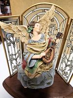 Vintage Hallmark Heavenly Minstrel angel figurine in color, holding a mandolin, in front of brass-filled glass triptych on dark wooden base.