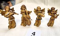 Front view showing all four standing cherub musical figurines, detailed gold robes, playing violin, cello, lute, and another string instrument.