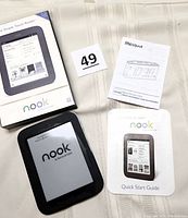 Barnes & Noble Nook eReader model BNRV300 with original box, quick start guide, and start guide on fabric surface