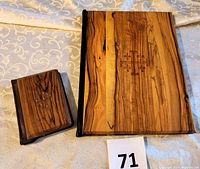 Photo showing two olive wood-covered New Testaments, the smaller Bible has a red leather spine and Jerusalem Cross on wood cover, the larger one is fully covered in wood with Jerusalem engraved.