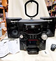 Full view of RCA stereo system including main unit, two speakers, antenna, remote, and manual on table.