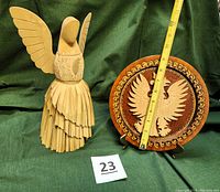 Photo of the straw angel figurine standing next to the Polish eagle decorative plate with measuring tape showing approximate sizes and lot tag 23.
