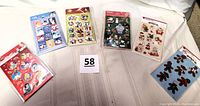 Overview photo showing all six packages of holiday stickers featuring various Christmas themes and characters laid out on a fabric surface.
