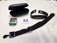 Cycle monitor unit, chest strap, adjustable fabric strap, and black zippered hard case on white cloth background with lot number card