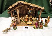 Front view of nativity set showing wooden stable with ceramic figurines arranged in front and inside, including Holy Family, three wise men, shepherd, angel, ox, donkey, and sheep.