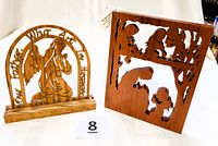 Photo showing two wood-cut religious art pieces: a praying angel in arch with inscription and a cherry wood panel with Mary and baby Jesus.