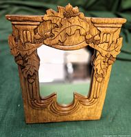 Front view of hand-carved oak leaf and acorn wooden framed mirror on stand, showing wood grain and carving detail