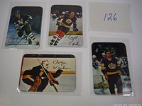 Four vintage 1977 Topps glossy hockey cards, each in protective sleeves, showing players from different NHL teams in action, with facsimile signatures below the player images.