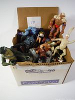 Box of assorted vintage toys and action figures showing various characters and vehicles packed inside a cardboard box.