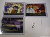 Three Pokemon special insert cards displayed on a white surface, each card shows scene from an early Pokemon episode, protected in plastic sleeves.