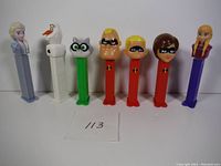 Photo showing seven PEZ dispensers in a row with characters from Frozen and The Incredibles, plus a raccoon.