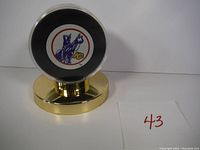 Front side of the hockey puck showing Kansas City Scouts logo mounted on gold-colored display stand with sticker residue visible.