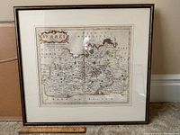 Full view of framed antique map of Surrey leaning against a wall with a measuring stick indicating size.