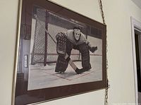 Framed print hung on wall showing the hockey goalie in front of the net in a defensive stance.