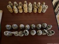 Top-down view of all chess pieces arranged in two rows by color set on a brown wooden surface.