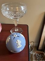 Clear crystal candy bowl with cut patterns and three round blue Wedgwood spheres decorated with white cherubs and floral reliefs.