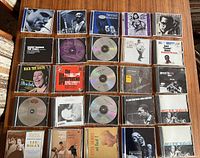 Photo showing top view of the 25 jazz CDs laid out on a wooden surface displaying cover art featuring Miles Davis, Ella Fitzgerald, Etta James and more.