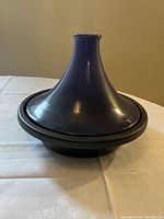 Closed view of the Le Creuset oven with purple conical lid sitting on a white cloth surface against beige background.