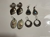 Four pairs of Mexican silver earrings laid out showing front sides with various designs and materials.