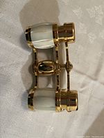 Gold and white colored opera glasses showing the side and body with gold metal and white accents.