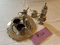 Overview of scalloped tray holding two mustard pots (one lid open), two salt cellars, pair of salt and pepper shakers, plus sugar caster on right