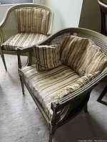 Two reproduction arm chairs with cane sides and backs, floral striped cushions and square pillows, placed on carpet.