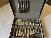 Photo showing full selection of flatware pieces inside a storage box on a tablecloth.