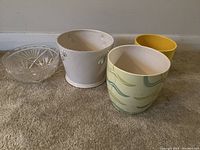 View from front showing all four items on floor: three ceramic planters and one glass bowl.
