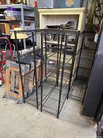 Three black wire rack shelving units shown in a storage or garage area with other items around them.