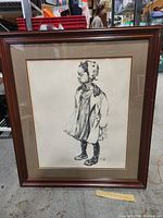 Framed artwork featuring black ink sketch of a child in profile wearing a bonnet and dress, framed in dark wood with dual matting.