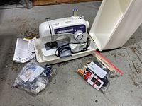 Full view of Brother XL-2600i sewing machine in carrying case with foot pedal, manual, and two clear bags of assorted sewing notions.