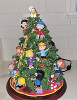 Front view of lit Peanuts Christmas tree on wooden base with Snoopy, Lucy, Charlie Brown, Sally, and Schroeder figures