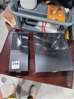 Two Donna Karan boxes on a wooden surface containing bedding items with visible floral design on one of the sheets in black.