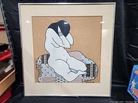 Full frontal photo of the fabric artwork in frame, showing the reclining nude woman on patterned fabric cushion against a plain brown fabric background.