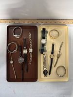10 ladies wristwatches displayed in two trays on a white surface with a ruler behind for scale
