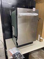 Front view of 18" Honeywell stainless steel dishwasher with protective wrapping showing minor dent on top lid