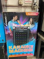Photo of the product box front showing a man and woman singing with the Masingo Soprano X1 karaoke machine and listing main features.