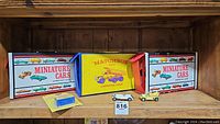 Three vintage Matchbox and Miniature Car carrying cases stacked and displayed with loose miniature cars in front of them.
