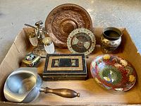 Wide view showing entire lot of metal decorative and functional items inside a box including peacock bowl, incense burner, calendar, vase and more.