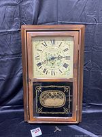 Front view of rectangular wooden wall clock with glass door closed showing floral dial and decorative lower panel.