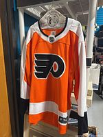 Front view of orange, white, and black Philadelphia Flyers hockey jersey with NHL logo on collar and large Flyers logo on chest.