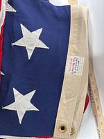 Close-up of older cotton flag showing sewn white stars on blue field and label indicating Valley Forge Flag Company, Spring City PA.