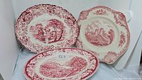 Three assorted vintage porcelain platters shown together, showing the different shapes and red white transferware scenes.